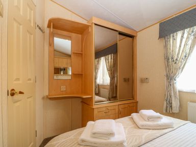A bedroom with a bed with folded towels a wooden vanity unit with mirror and window with curtains at Cae Gog Near Cemaes Bay
