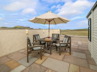 An outdoor patio with a wooden table and four chairs under a large umbrella at Cae Gog Near Cemaes Bay