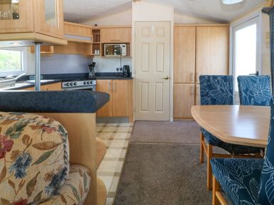 A kitchen and dining area with wooden cabinets a stove and blue patterned chairs at Cae Carreg in Cemaes Bay