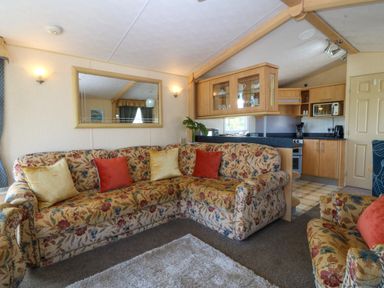 A living room with floral patterned sofas and cushions next to a kitchen with wooden cabinets at Cae Carreg in Cemaes Bay