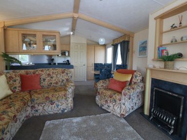 A living room with floral sofas a fireplace a dining table with chairs and kitchen cabinets at Cae Carreg in Cemaes Bay