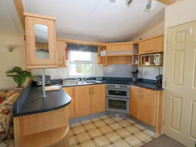 A kitchen with wooden cabinets a double oven a sink a microwave and a window at Cae Carreg in Cemaes Bay