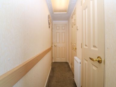 A hallway with multiple closed doors a radiator and a wooden handrail at Cae Carreg in Cemaes Bay