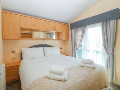A bedroom with a bed with white linens and folded towels next to a window with curtains at Cae Carreg in Cemaes Bay