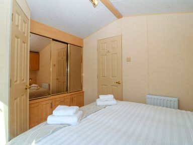A bedroom with a bed with folded towels on it and mirrored wardrobes at Cae Carreg in Cemaes Bay
