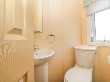 A small bathroom with a pedestal sink a toilet a window with a printed blind and a beige door at Cae Carreg in Cemaes Bay