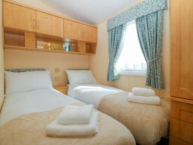 A bedroom with two single beds with folded towels and wooden cabinets at Cae Carreg in Cemaes Bay