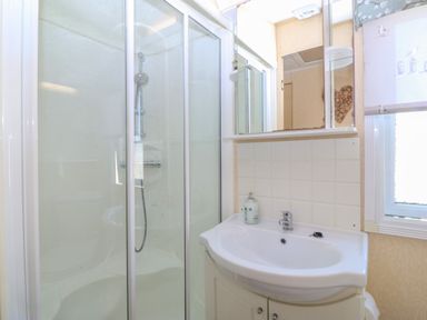 A bathroom with a shower enclosure a sink with a cabinet soap dispenser and a mirror at Cae Carreg in Cemaes Bay
