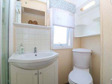 A small bathroom with a sink and mirror above it a toilet and a window with a patterned blind at Cae Carreg in Cemaes Bay