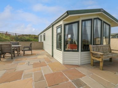 A patio area with wooden chairs and table beside a mobile home at Cae Carreg in Cemaes Bay