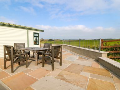 An outdoor patio with a wooden table and four chairs next to a cream building at Cae Carreg in Cemaes Bay