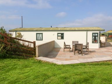 A patio with wooden table and chairs outside a white building with green trim at Cae Carreg in Cemaes Bay
