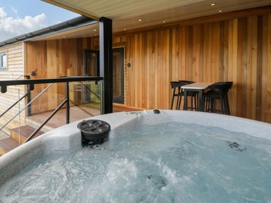 An outdoor hot tub on a wooden deck with a table and four chairs at Betsi Lodge 1 in Llanelidan near Corwen
