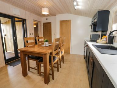 A kitchen and dining area with a wooden table and chairs next to black cabinets and a sink at Betsi Lodge 1 in Llanelidan near Corwen
