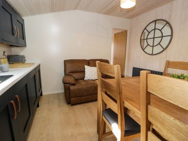 A kitchen and dining area with black cabinets a brown sofa and a wooden dining table with chairs at Betsi Lodge 1 Llanelidan near Corwen