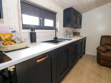 A kitchen counter with black cabinets a sink window knife holder and snacks next to a brown armchair at Betsi Lodge 1 Llanelidan near Corwen