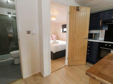 A kitchen with dark cabinets and a microwave next to a partially open door showing a bedroom with a bed and folded towels at Betsi Lodge 1 Llanelidan near Corwen