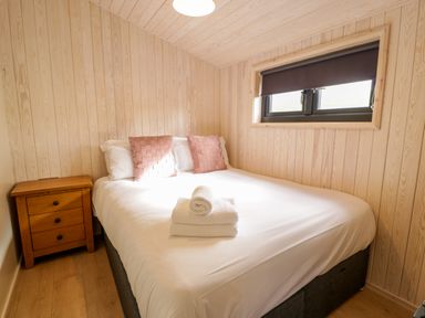 A bedroom with a double bed white sheets two pink pillows wooden nightstand and a window with a blind at Betsi Lodge 1 Llanelidan near Corwen