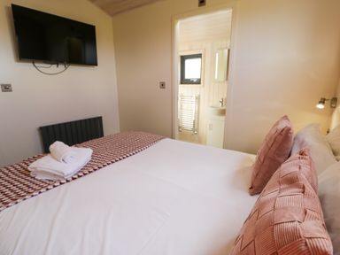 A bedroom with a bed with pillows and folded towels and a wall mounted tv at Betsi Lodge 1 Llanelidan near Corwen