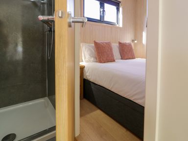 A bedroom with a bed and pink pillows next to a shower area at Betsi (Lodge 1) in Llanelidan near Corwen