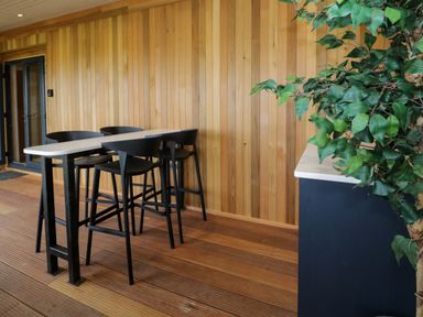 A dining area with a tall table and four black chairs next to a wooden wall and a plant at Betsi Lodge 1 in Llanelidan near Corwen