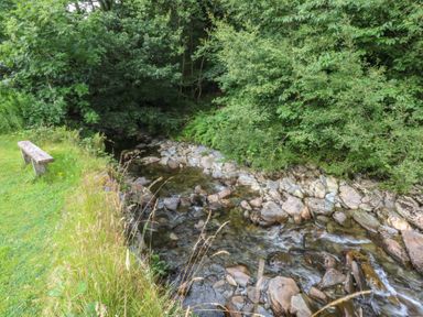 A stream with stones and a bench by the water at Chandos in Dolwyddelan