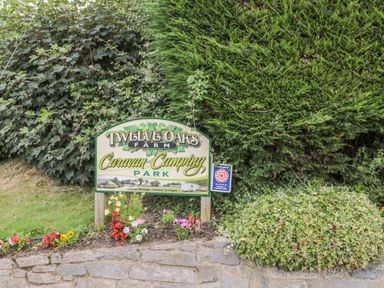 A sign for Twelve Oaks Farm Caravan and Camping Park with flowers and bushes surrounding it at Hazel Lodge in Teigngrace near Newton Abbot