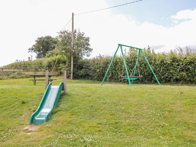 A playground with a green slide and a swing set on grass near trees and bushes at Hazel Lodge in Teigngrace near Newton Abbot