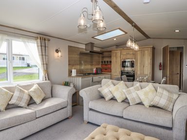 A living room with sofas and cushions next to a kitchen with wooden cabinets and dining area at Hazel Lodge in Teigngrace near Newton Abbot