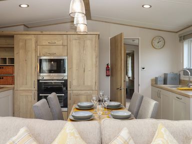 A kitchen and dining area with wooden cabinets a dining table set with plates glasses and gray chairs at Hazel Lodge Teigngrace near Newton Abbot