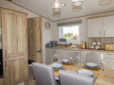 A dining table set with plates and wine glasses in a kitchen with wooden cabinets and a window at Hazel Lodge Teigngrace near Newton Abbot