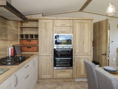 A kitchen area with built-in oven and microwave wooden cabinets stove and grey dining chairs at Hazel Lodge in Teigngrace near Newton Abbot