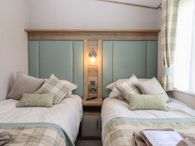 A bedroom with two single beds with pillows and blankets and a bedside table with a lamp at Hazel Lodge in Teigngrace near Newton Abbot
