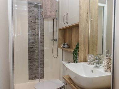 A bathroom with a shower enclosure a toilet a sink and wooden cabinets at Hazel Lodge in Teigngrace near Newton Abbot