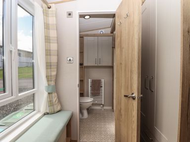 A small bathroom with a toilet towel radiator cabinets and a window seat with curtains at Hazel Lodge in Teigngrace near Newton Abbot