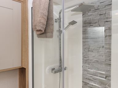 A shower area with a glass door a silver showerhead and stone tile wall at Hazel Lodge in Teigngrace near Newton Abbot
