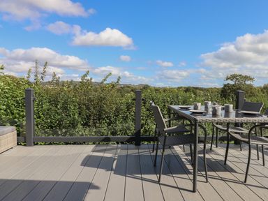 An outdoor patio with a table set for four and chairs overlooking greenery at Hazel Lodge in Teigngrace near Newton Abbot