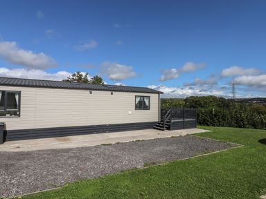 A beige mobile home with dark trim on grass and gravel with a small deck and railing at Hazel Lodge in Teigngrace near Newton Abbot
