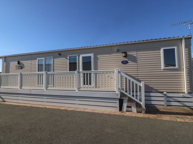 A beige mobile home with white railing and steps at Seafront Holiday Home 2 in Pwllheli