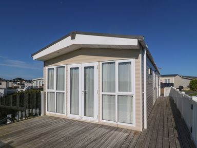 An exterior view of a beige static caravan with large white framed windows and doors on a wooden deck at Seafront Holiday Home 2 in Pwllheli