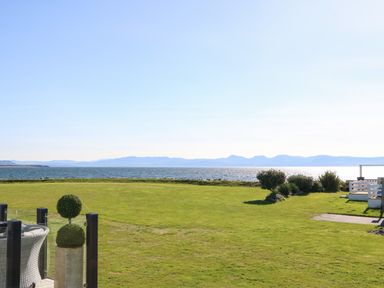 A large green lawn overlooking a body of water with distant mountains at Seafront Holiday Home 2 in Pwllheli