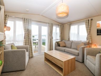 A living room with two armchairs a sofa a wooden coffee table and patterned curtains at Seafront Holiday Home 2 Pwllheli