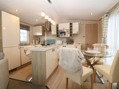 A modern kitchen and dining area with cream chairs and a glass table at Seafront Holiday Home 2 in Pwllheli