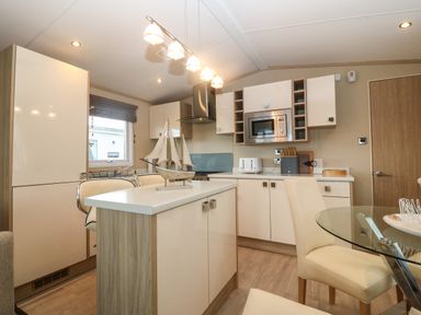A kitchen with an island, microwave, toaster, knives set, dining chairs, and a glass dining table at Seafront Holiday Home 2 in Pwllheli