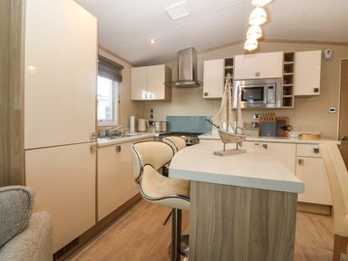 A kitchen with cream cabinets a countertop with bar stools a built in microwave and a decorative sailboat on the island at Seafront Holiday Home 2 Pwllheli