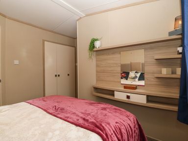 A bedroom with a bed covered with a white and pink blanket a wall-mounted wooden shelf with decorative items and a mirror at Seafront Holiday Home 2 Pwllheli