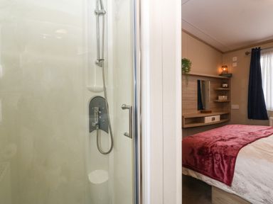 A shower cubicle with a handheld showerhead next to a bedroom with a bed and shelves at Seafront Holiday Home 2 Pwllheli