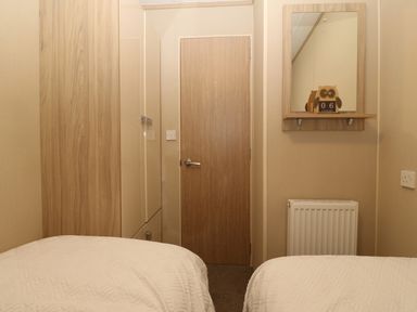 A bedroom with two beds a wooden door a wardrobe a wall mirror and a radiator at Seafront Holiday Home 2 in Pwllheli