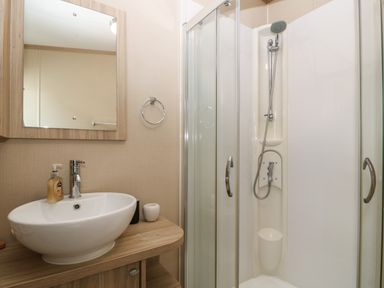 A bathroom with a sink and mirror beside a glass-enclosed shower at Seafront Holiday Home 2 in Pwllheli