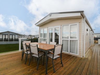 An outdoor wooden deck with a dining table and six chairs outside a mobile home at Seafront Holiday Home 2 in Pwllheli